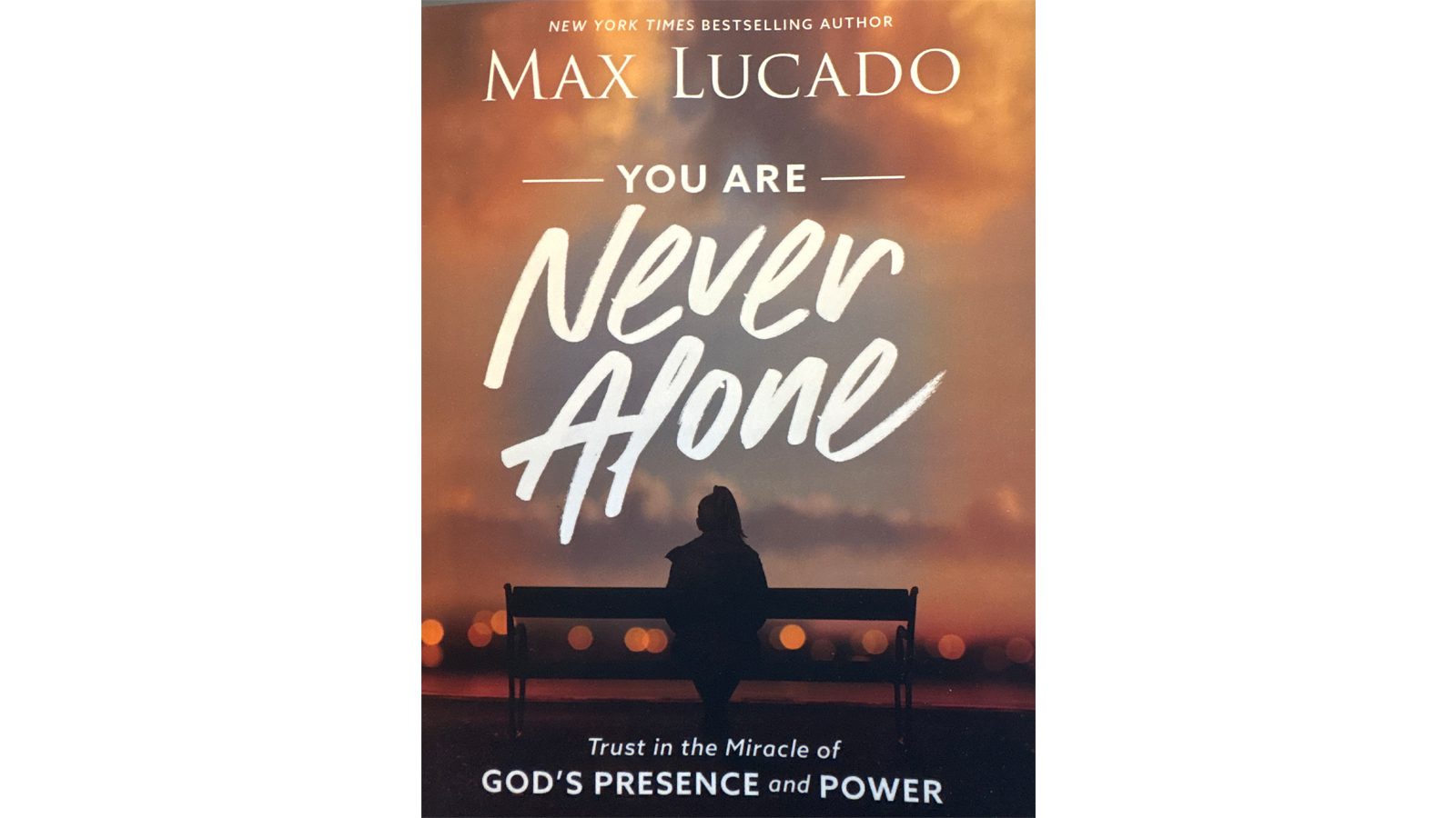Book cover of 'You Are Never Alone' by Max Lucado with a silhouette on a bench.