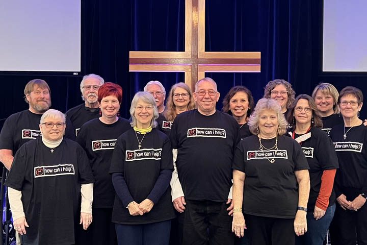 Group of people wearing matching shirts in front of a large cross.