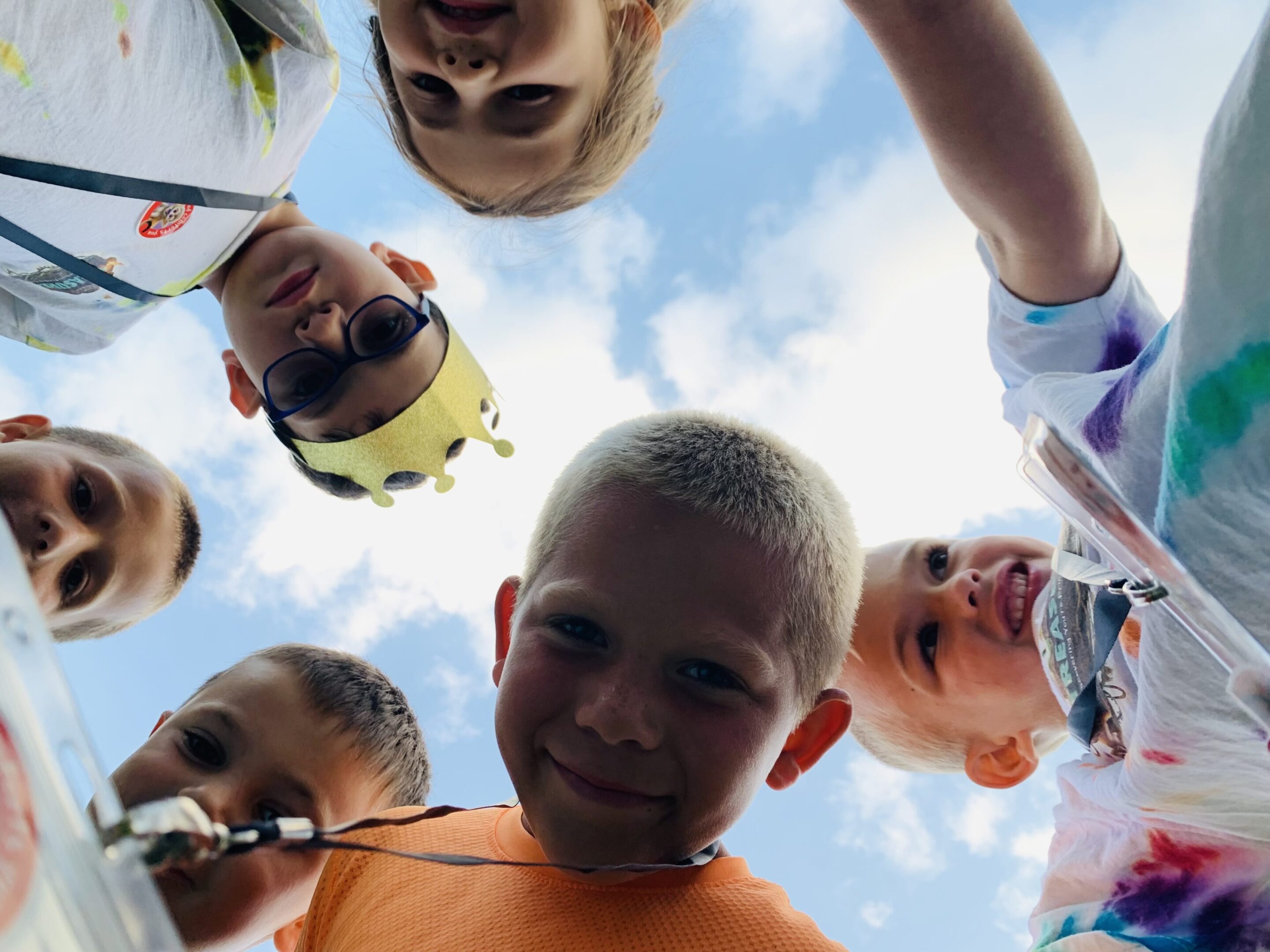 A group of kids smiling and looking down at the camera against a blue sky.