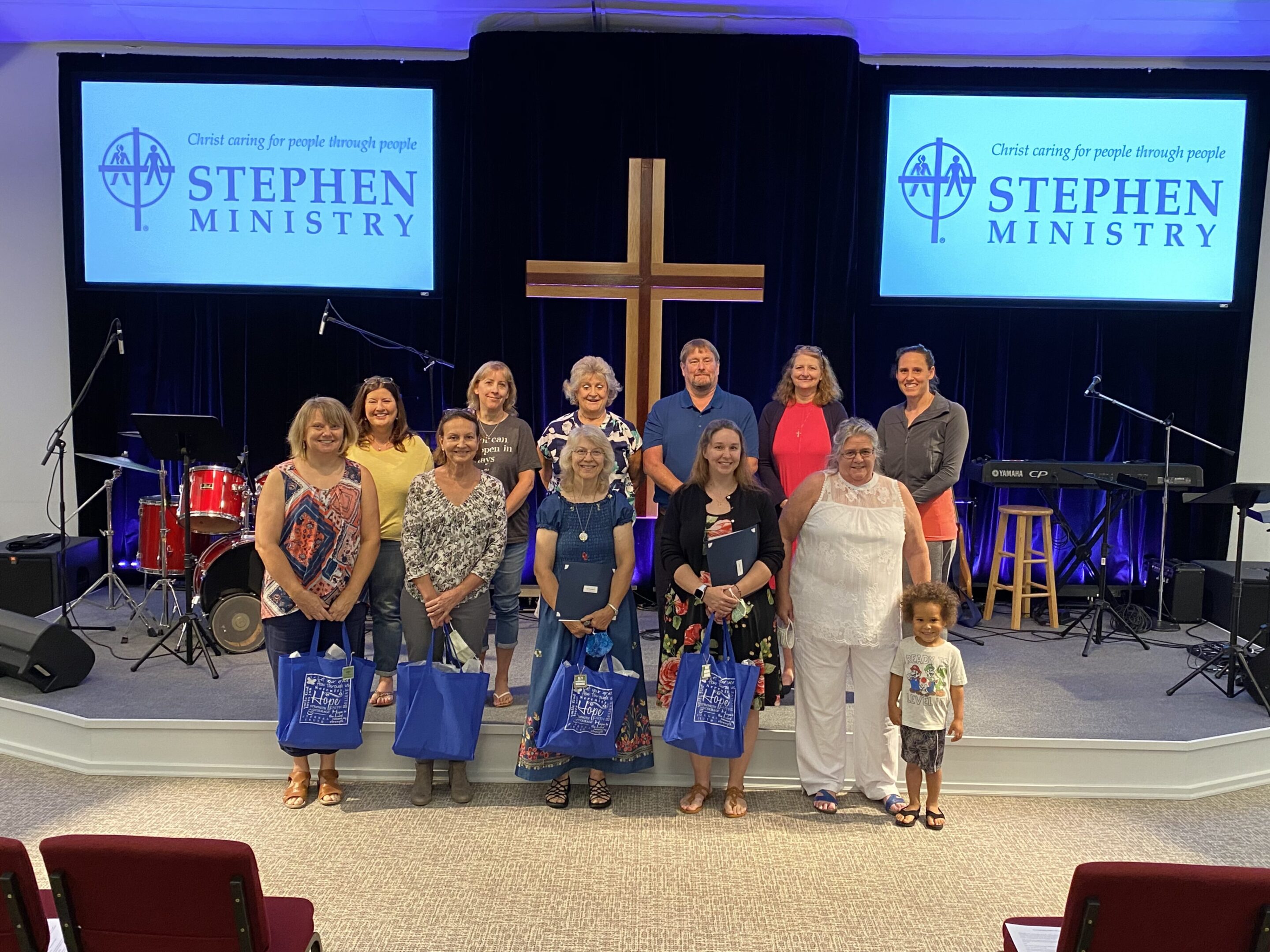 Group photo of people standing on a stage with a cross and Stephen Ministry banners.