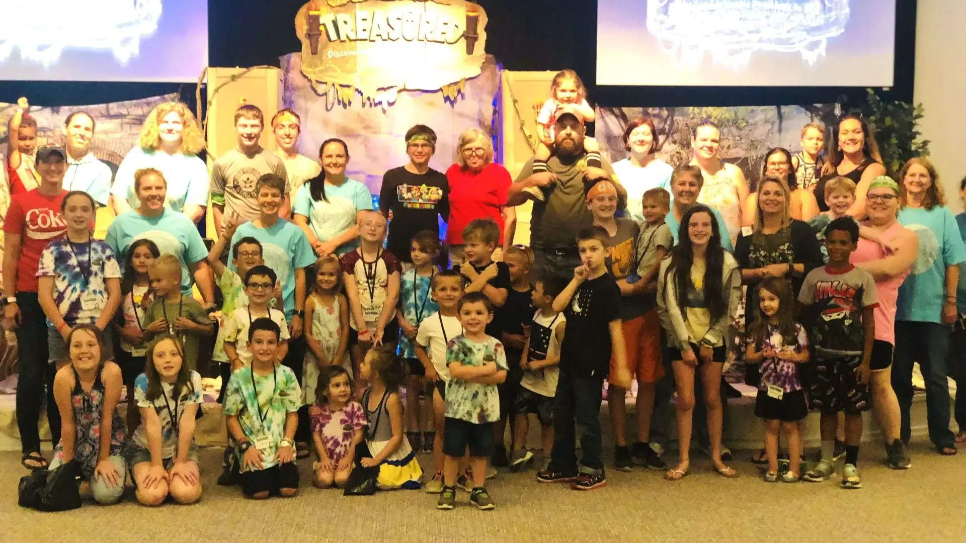Large group of children and adults smiling on stage at event.